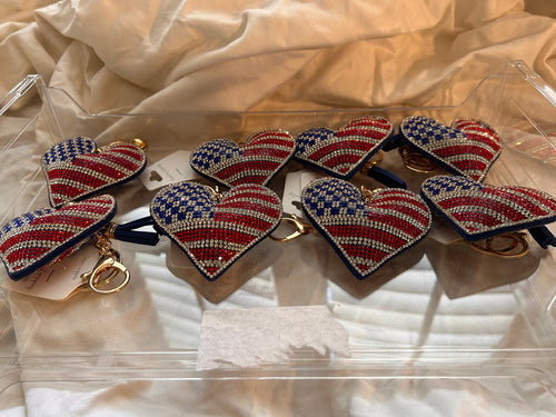 This Wrapables heart keychain features a puffy design adorned with red, white, and blue rhinestones forming an American flag pattern.It includes a gold-toned key ring, a lobster clasp for attachment to purses or handbags, and a dark blue tassel.The heart charm measures approximately 2.5 inches by 2.5 inches.The reverse side is made of a soft plush velvet material.